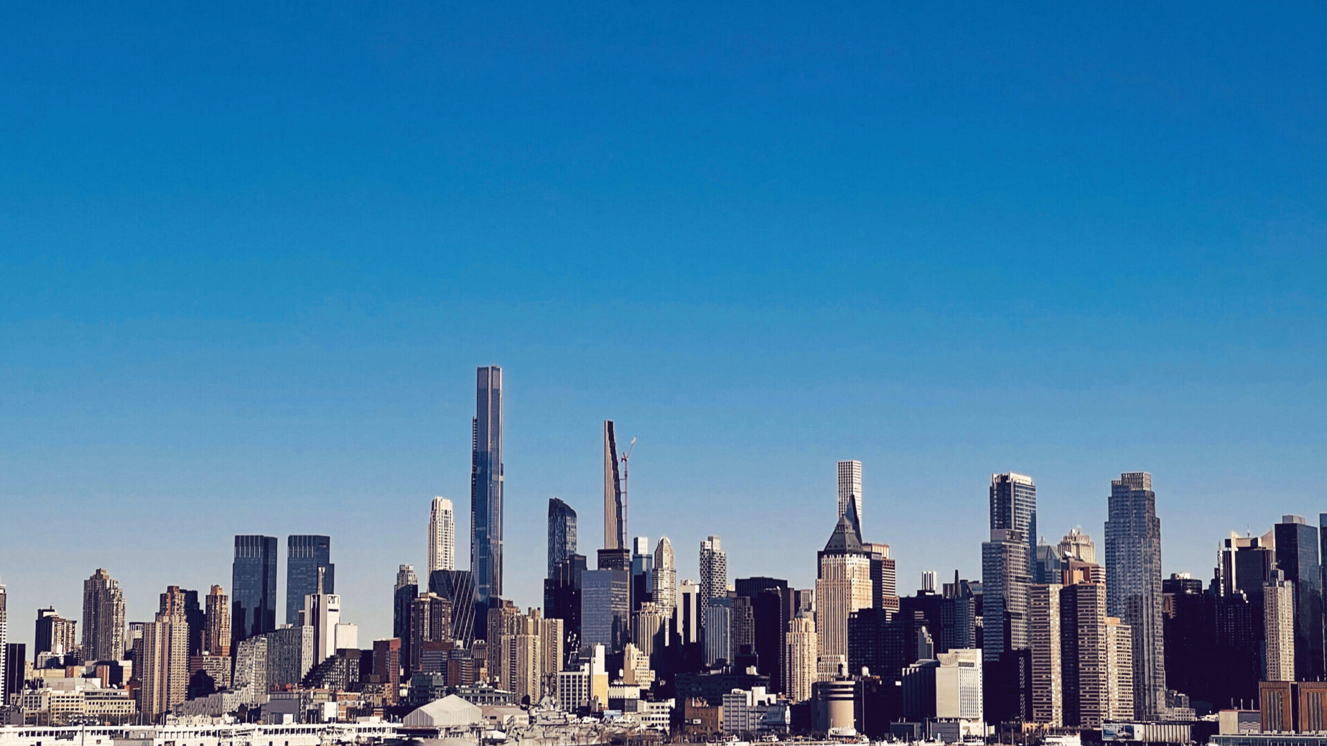 NYC skyline from the water with a deep blue sky that gets lighter as it approaches the skyline.
